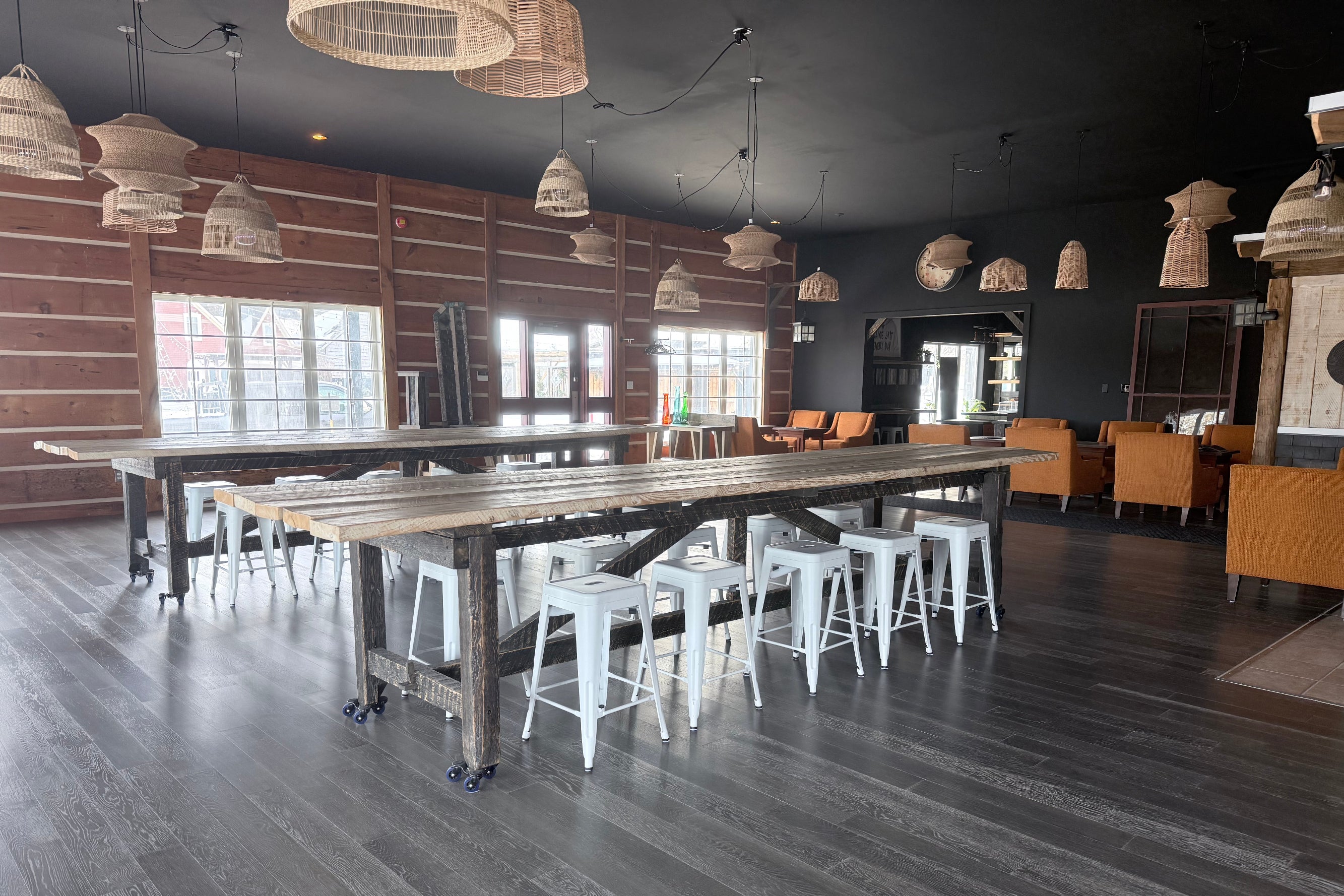 Large industrial-style room with wooden tables, stools, and pendant lights.