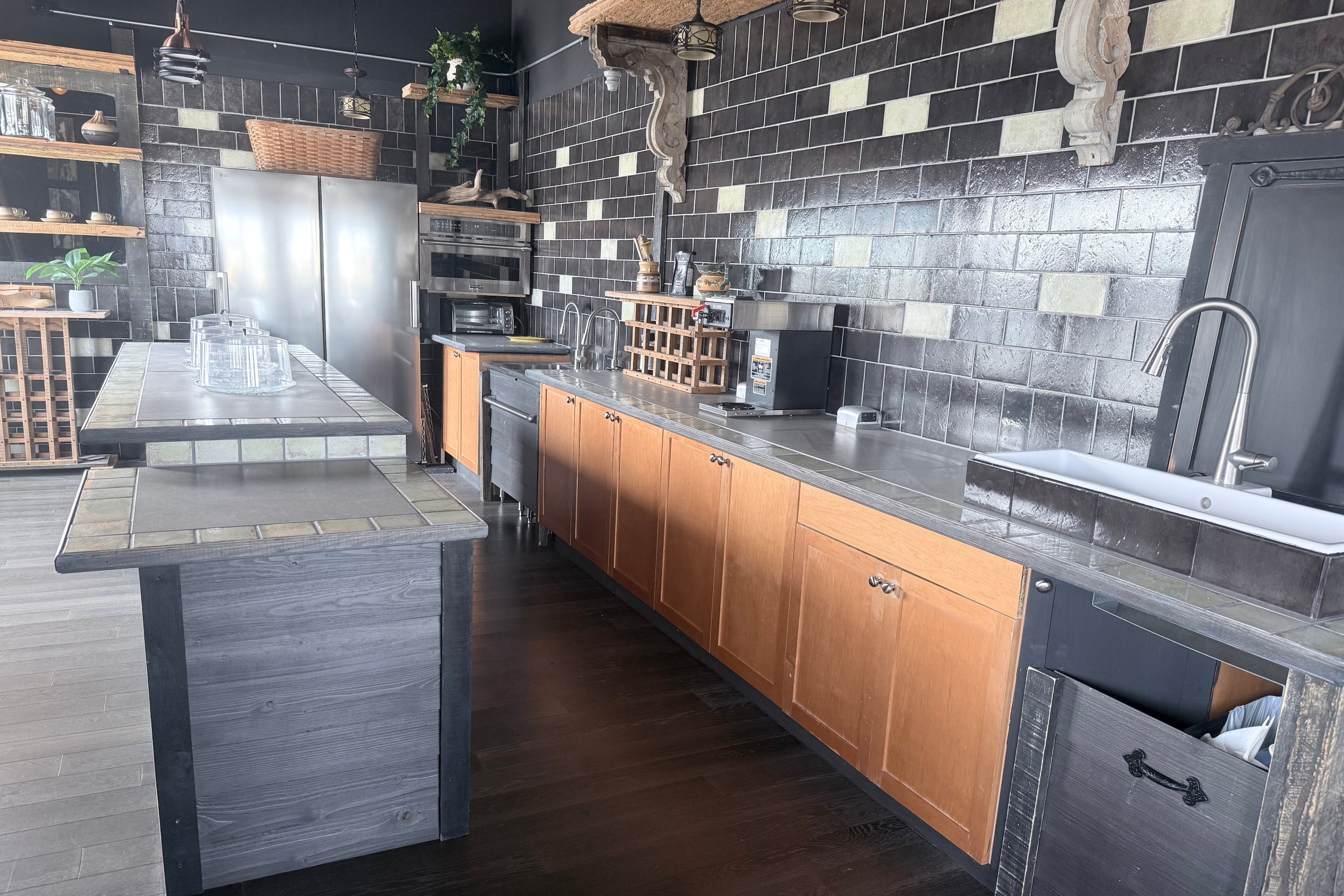Modern kitchen with wooden cabinets, stainless steel appliances, and black tiled walls.