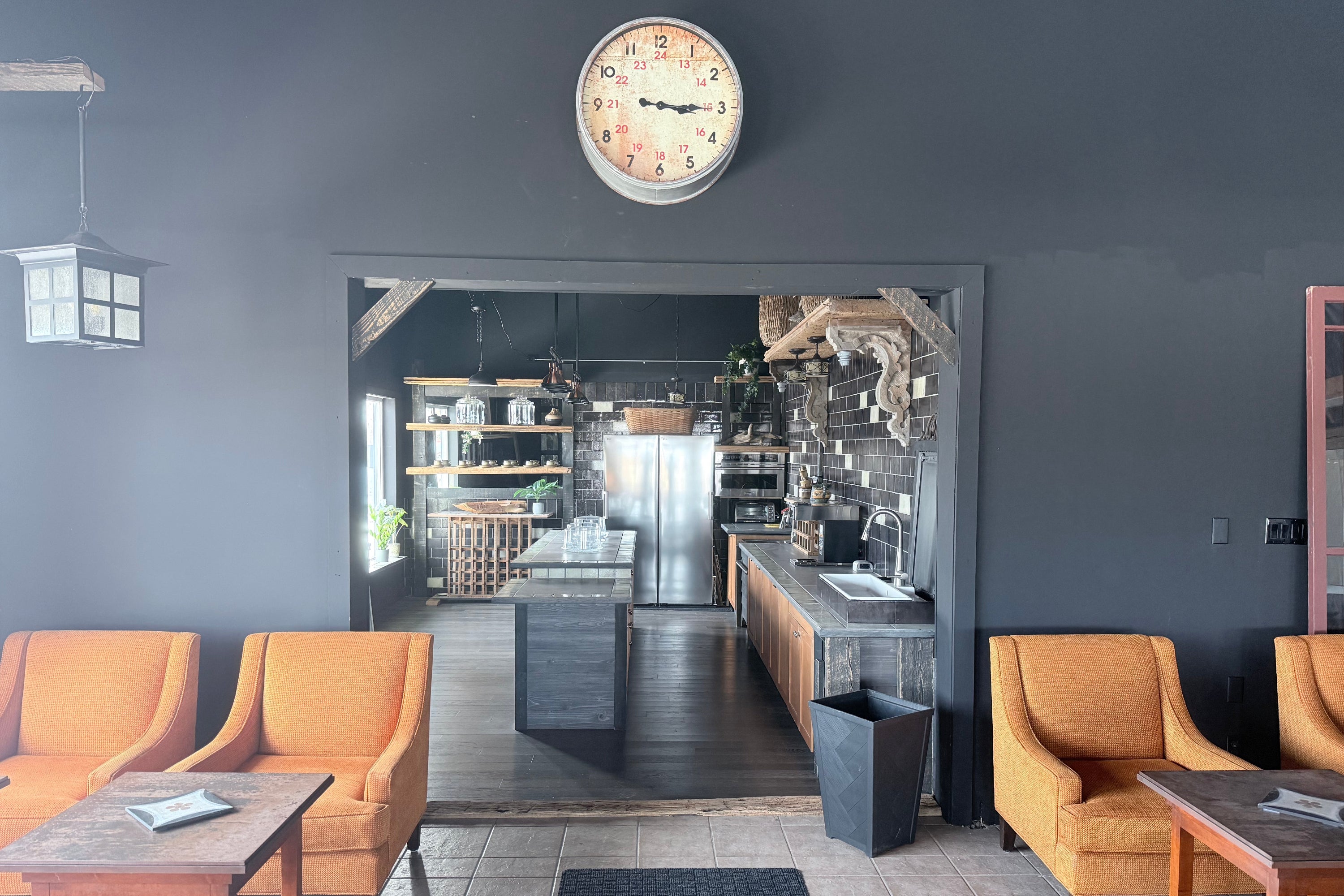 Modern interior with orange chairs, a clock on the wall, and a kitchen area.